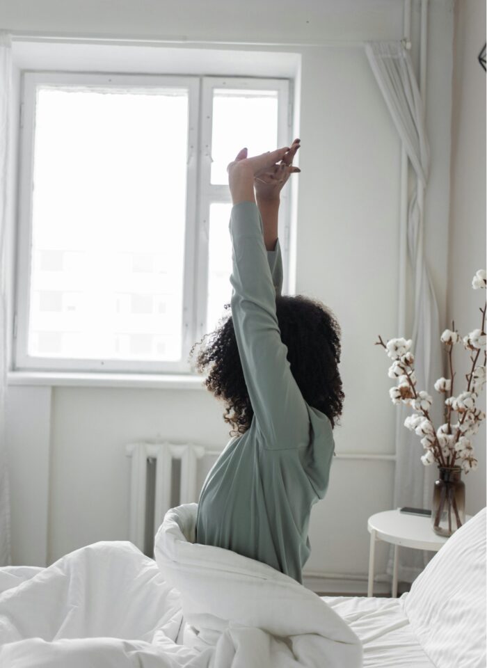 woman in bed in the morning stretching and looking towards the window
