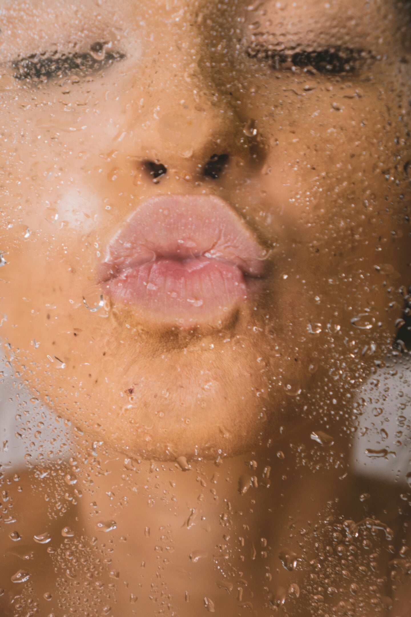 Woman with dewy skin pressing her face against a fogged-up glass, highlighting hydration from Korean skincare