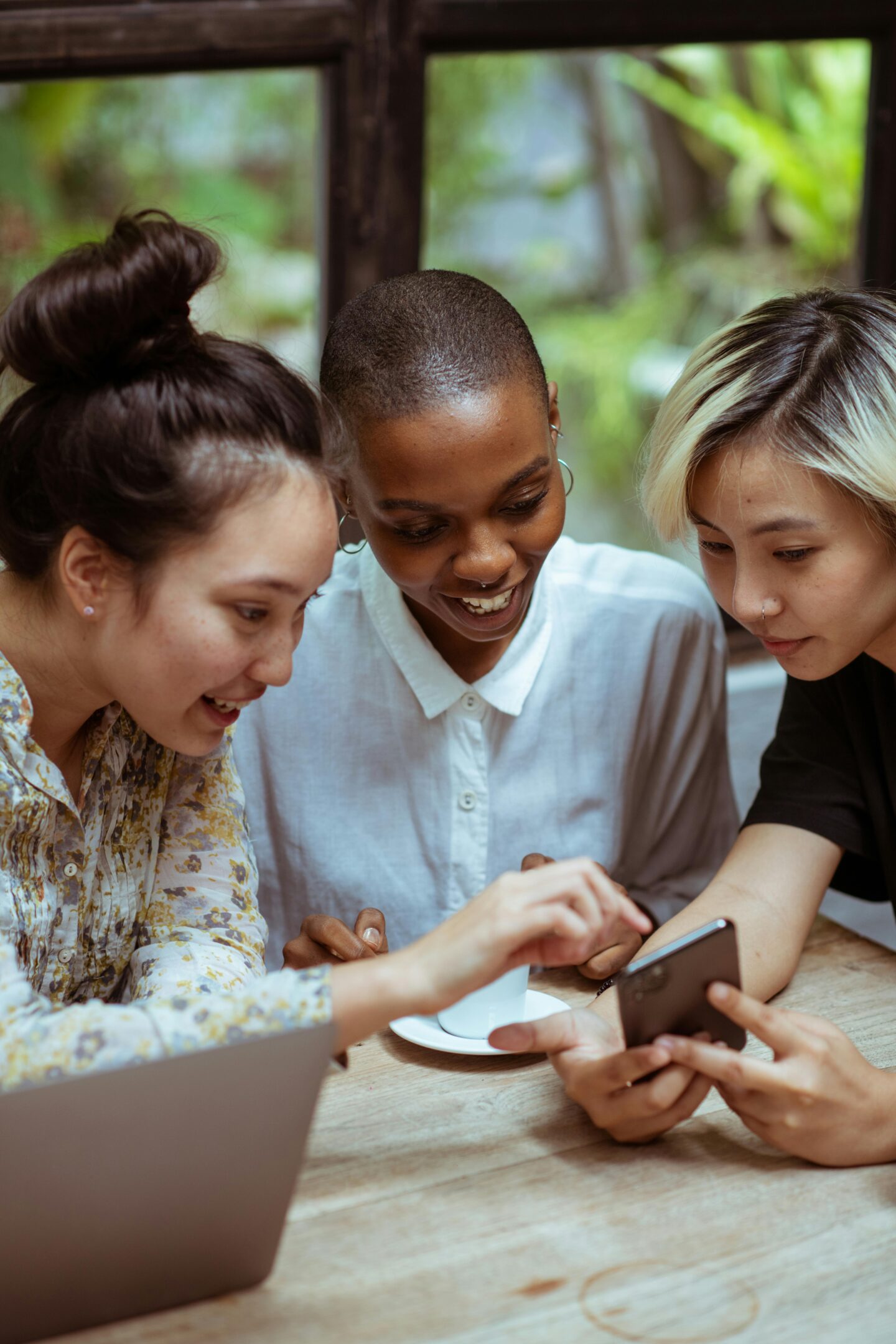 Three women smiling and engaging over a smartphone, focusing on brand monitoring and tracking online community mentions.