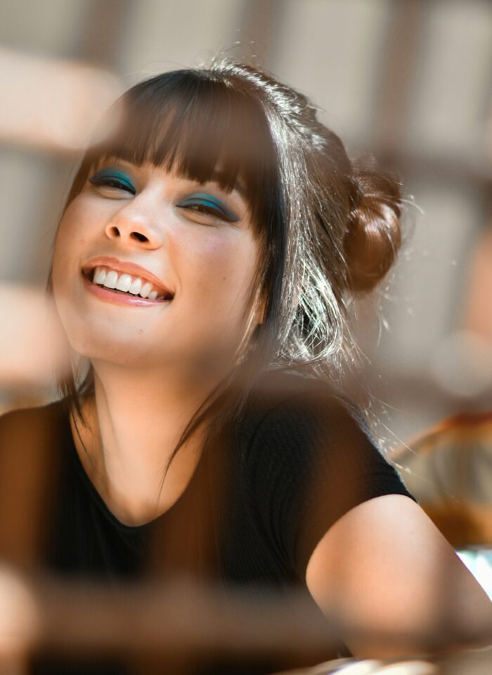Young woman with blue eye makeup smiling brightly, showing her teeth.