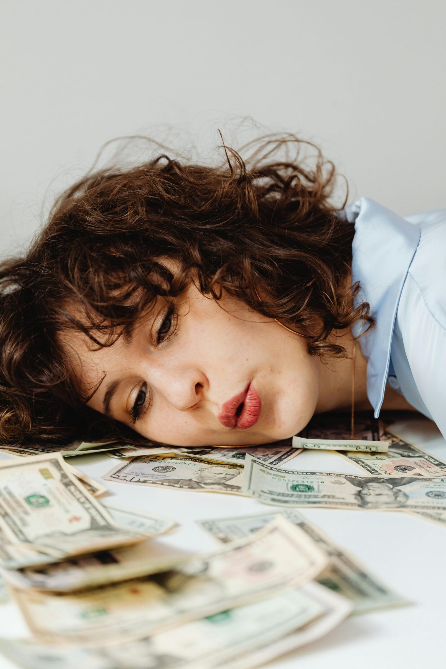 Young woman with curly hair lying on a pile of U.S. dollar bills, symbolizing business finances.