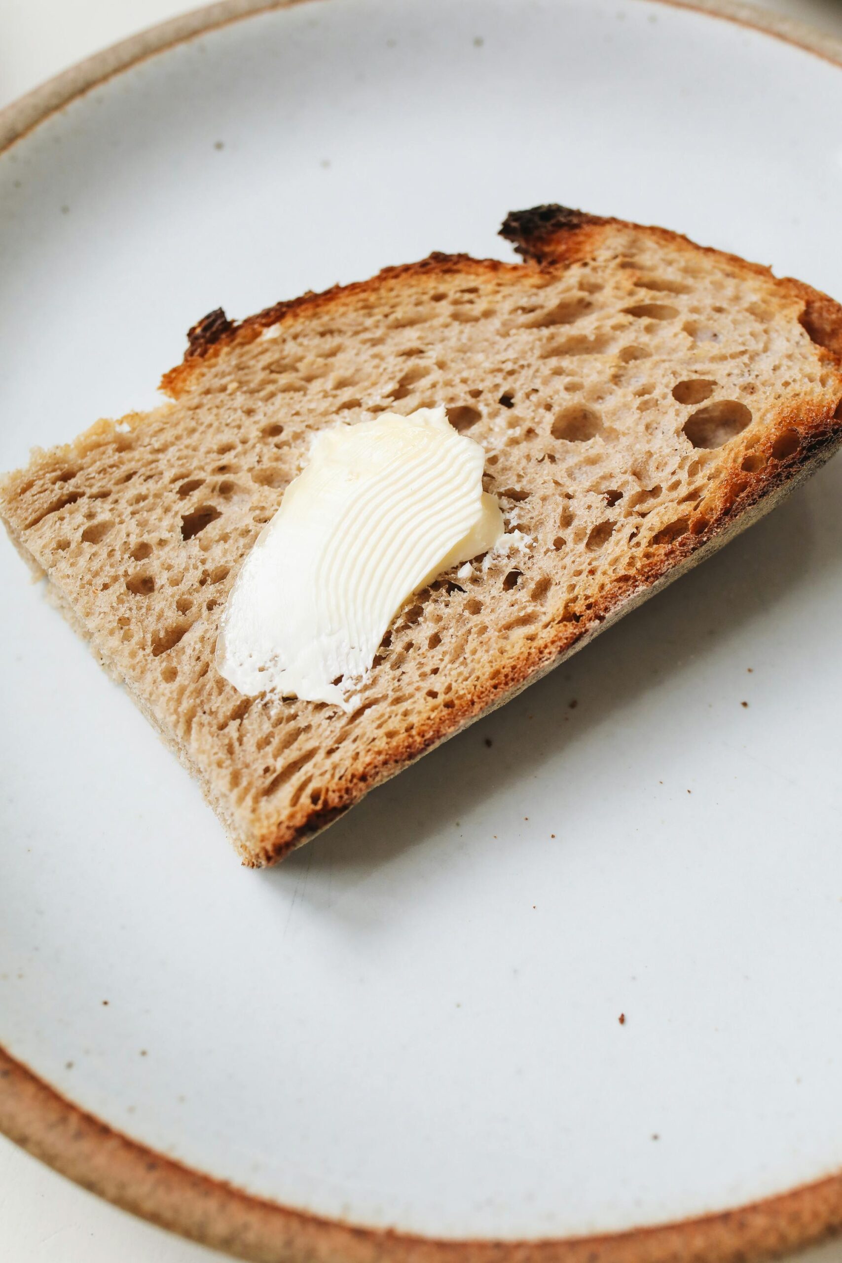 A slice of whole grain bread with a curl of butter spread on top, served on a white ceramic plate.