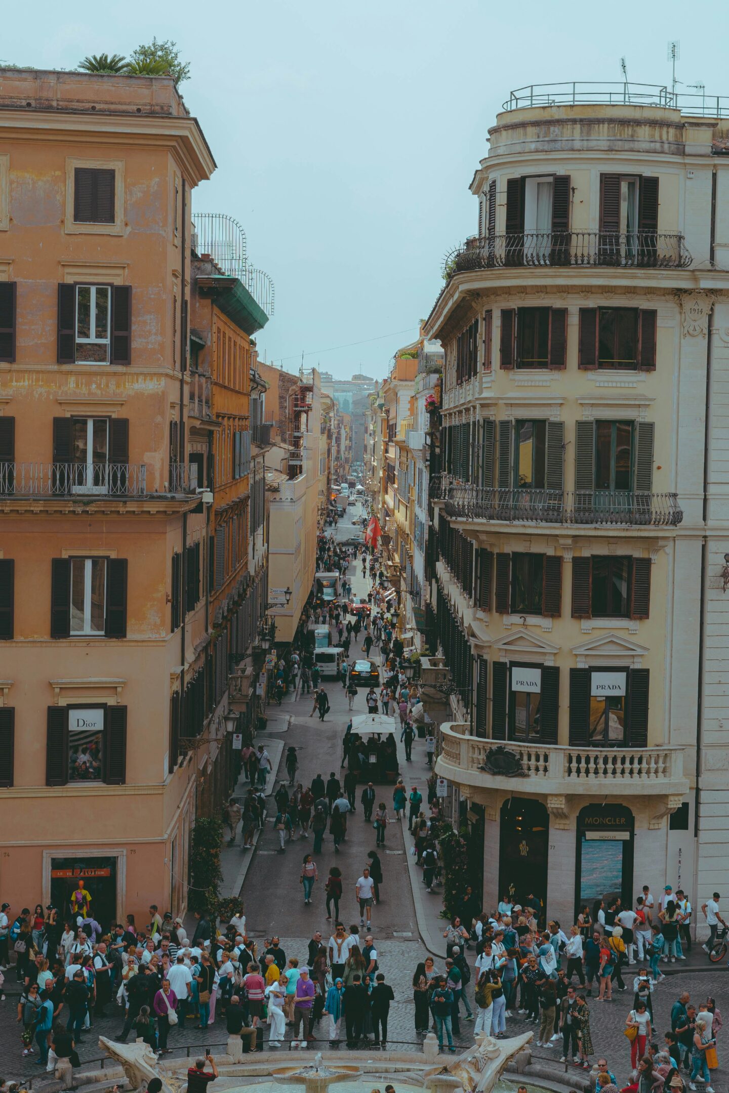Aerial view of a busy shopping street in Rome, Italy, surrounded by historic buildings and luxury brand stores.