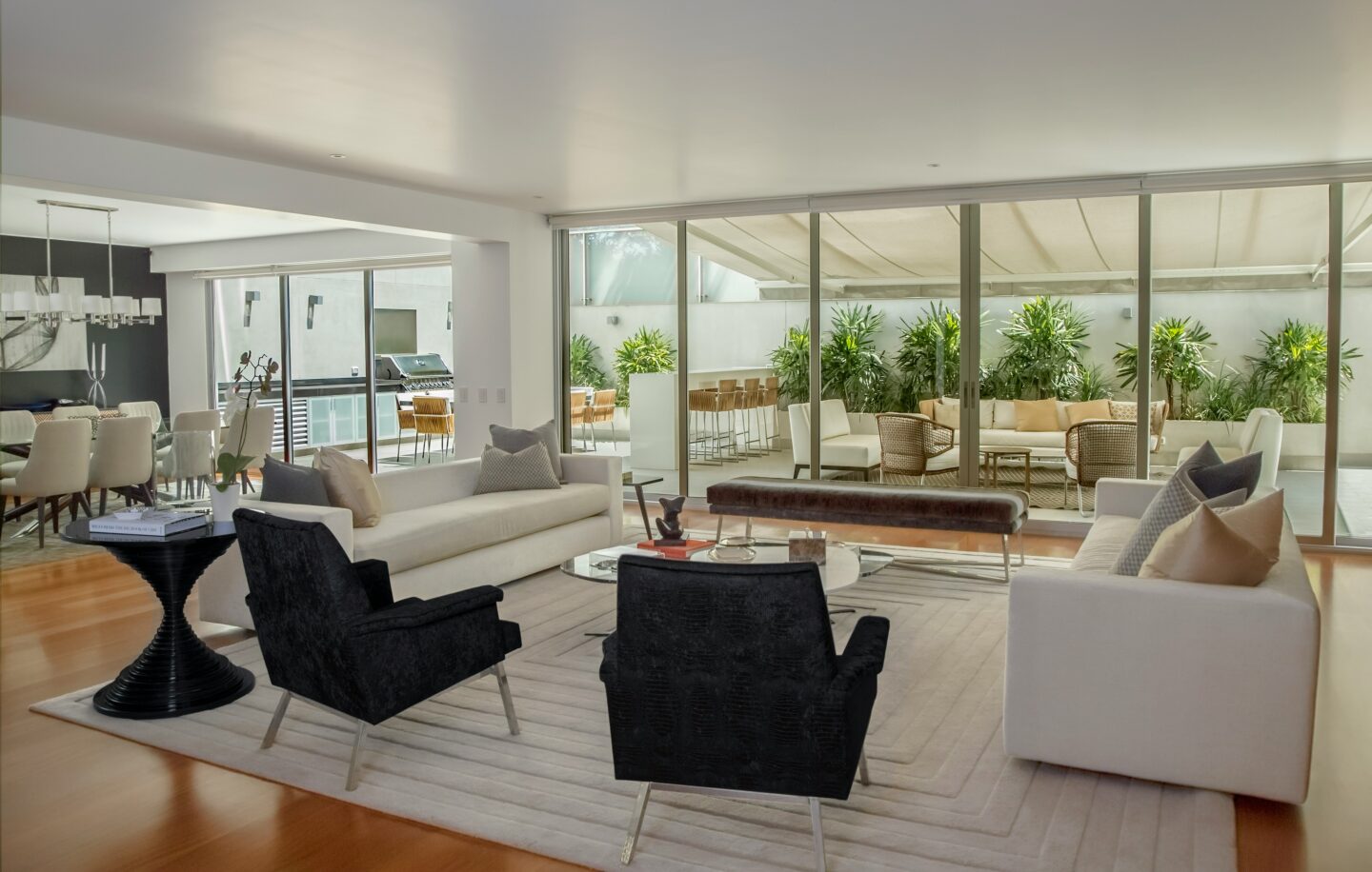 Spacious modern living room with symmetrical furniture arrangement and floor-to-ceiling glass doors leading to a balanced patio layout.