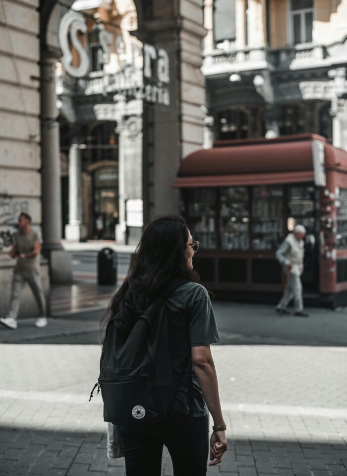 Woman walking with a backpack through a historic European shopping arcade in warm afternoon light.