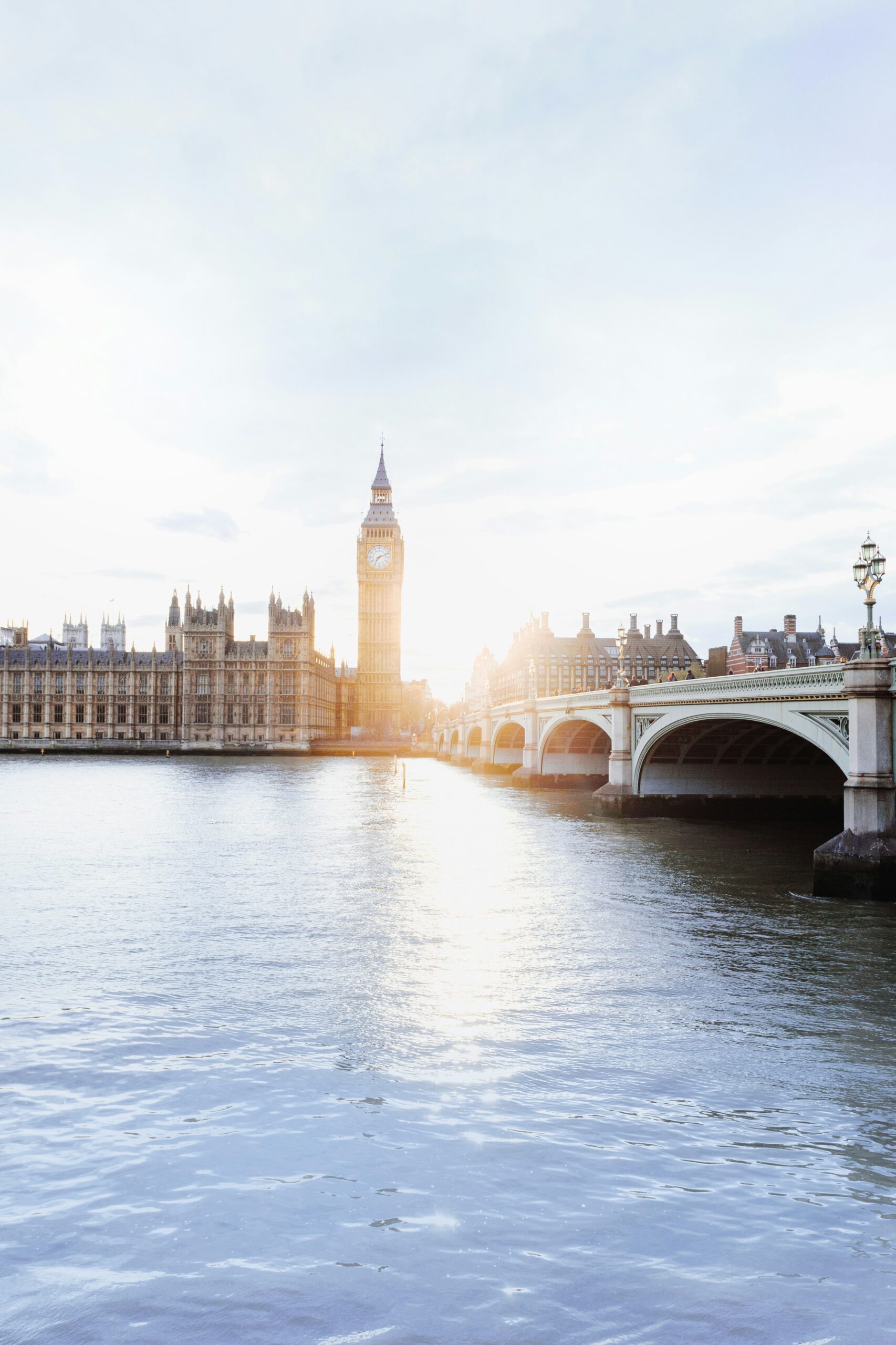 Sunlight shining behind Big Ben and the Houses of Parliament, with Westminster Bridge crossing the River Thames in London.