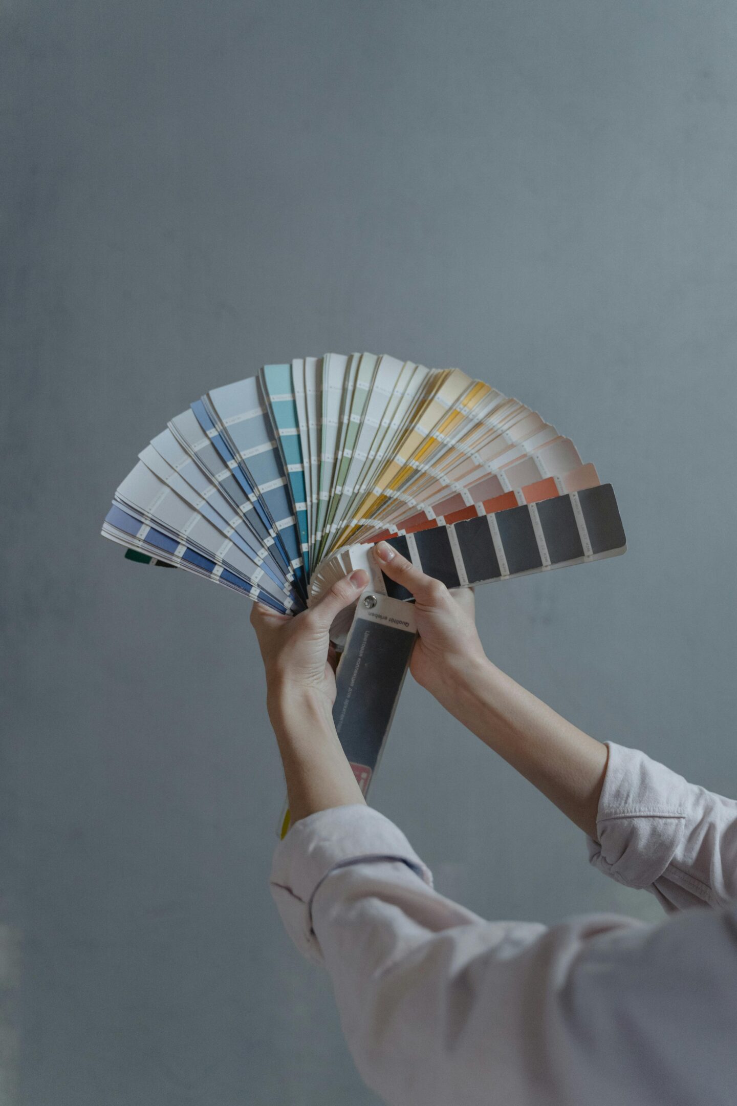 Interior design concept with hands holding a symmetrical fan of paint color swatches against a neutral wall—perfect for home makeover planning.