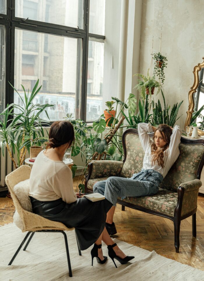 Psychotherapy session in a cozy, plant-filled room with two women engaging in mental health counseling and open conversation.