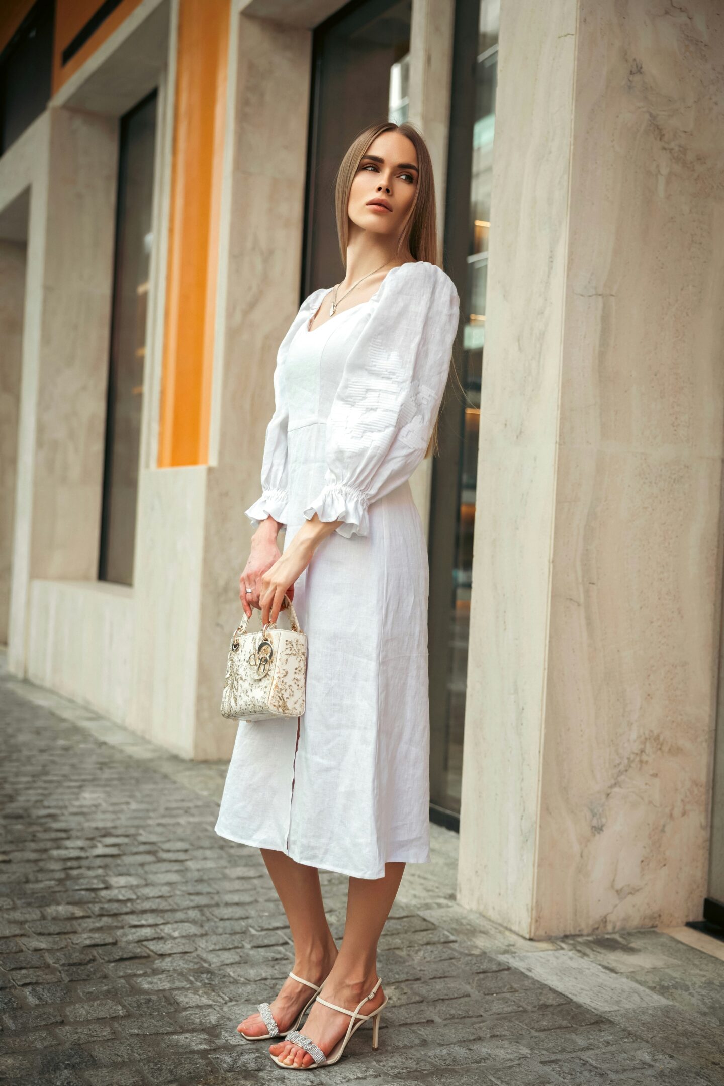 Elegant woman wearing a white linen midi dress and holding a small handbag, showcasing chic summer street style.