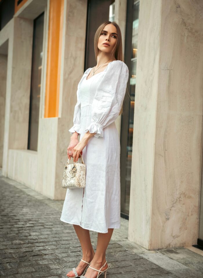 Elegant woman wearing a white linen midi dress and holding a small handbag, showcasing chic summer street style.