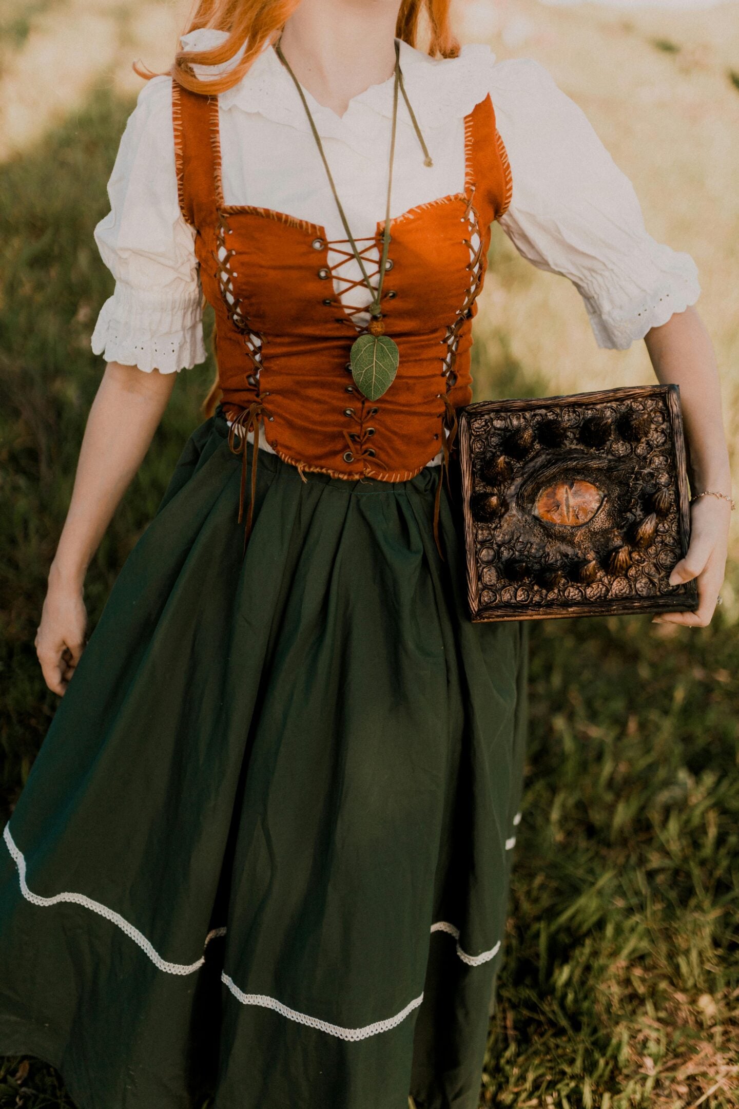 Renaissance fair costume with green skirt, orange corset, and fantasy prop book