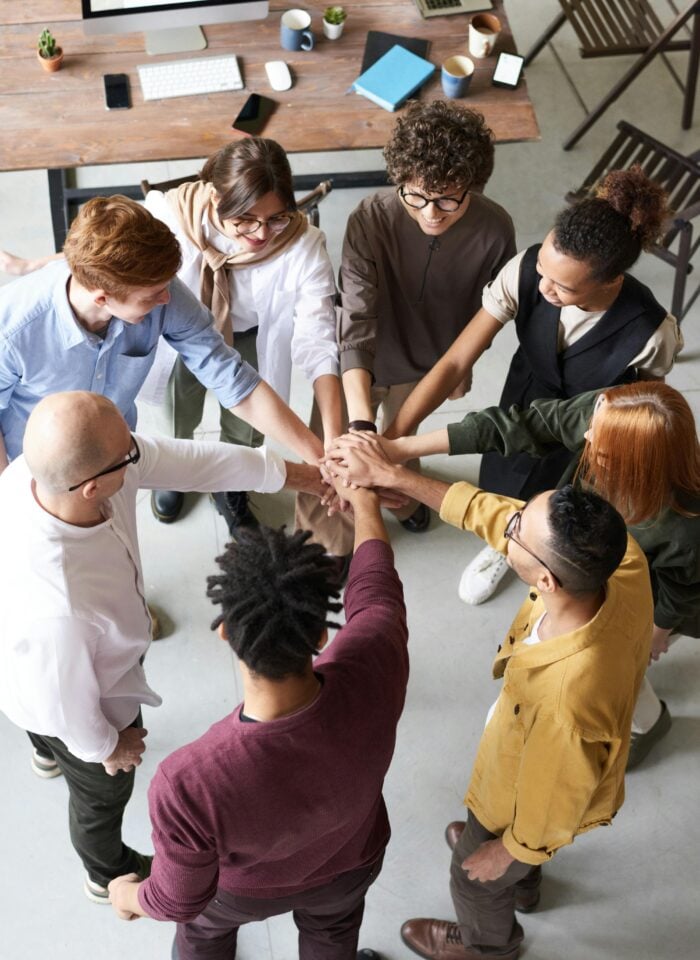 Employees stacking hands together in an office as a symbol of teamwork and collaboration during a team building exercise.