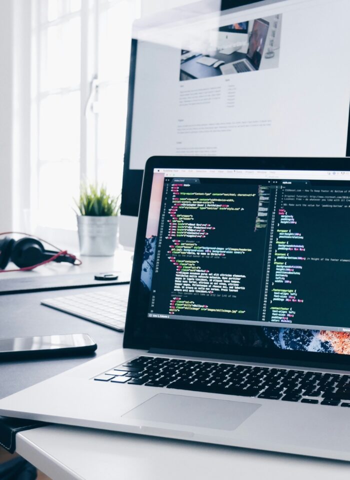 Modern workspace with a laptop displaying code, dual monitors, and web development tools, ideal setup for software developers or remote tech teams.