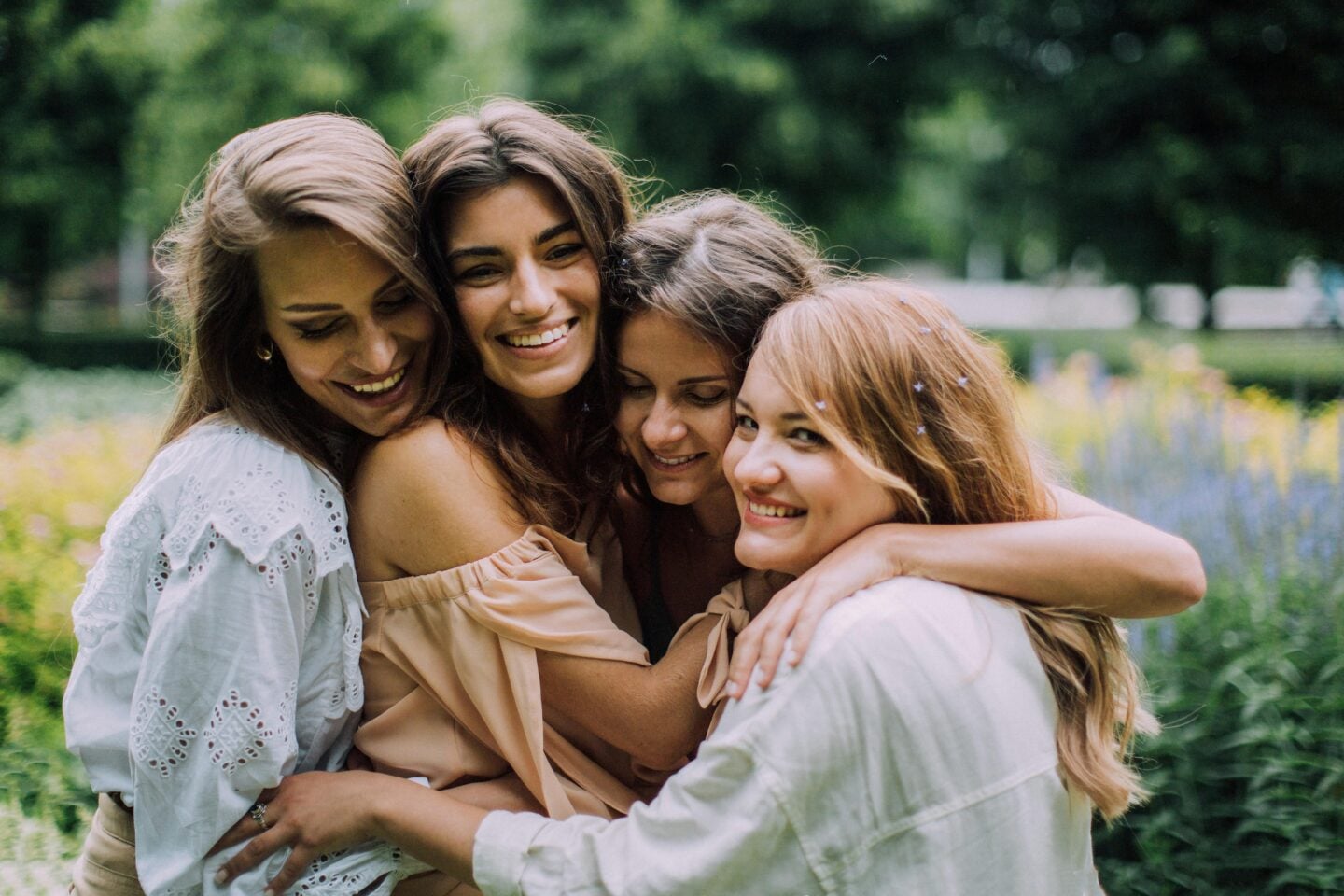 Group of four young women smiling and hugging each other closely in a lush garden, radiating joy and friendship.