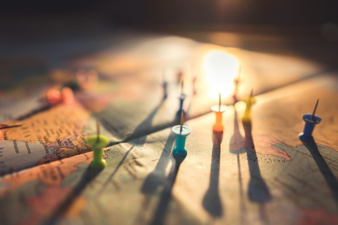 Close-up of a world map with colorful push pins marking different locations, illuminated by warm sunlight.