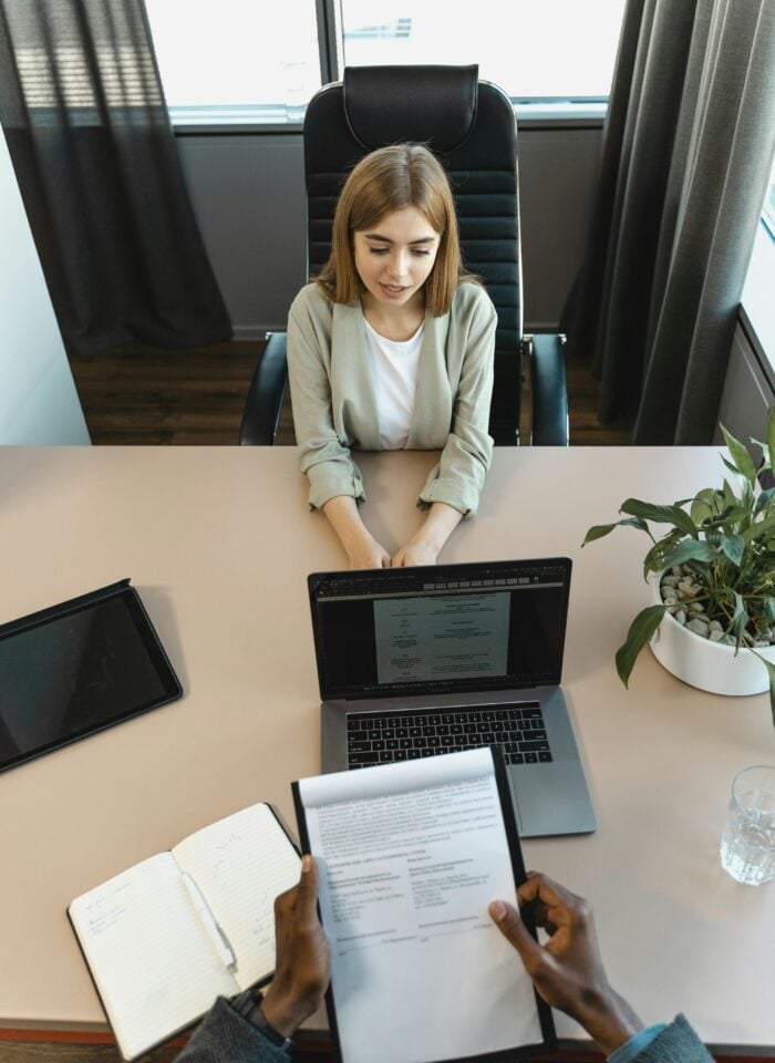 Young woman at a job interview sitting across from recruiter with resume and laptop on desk