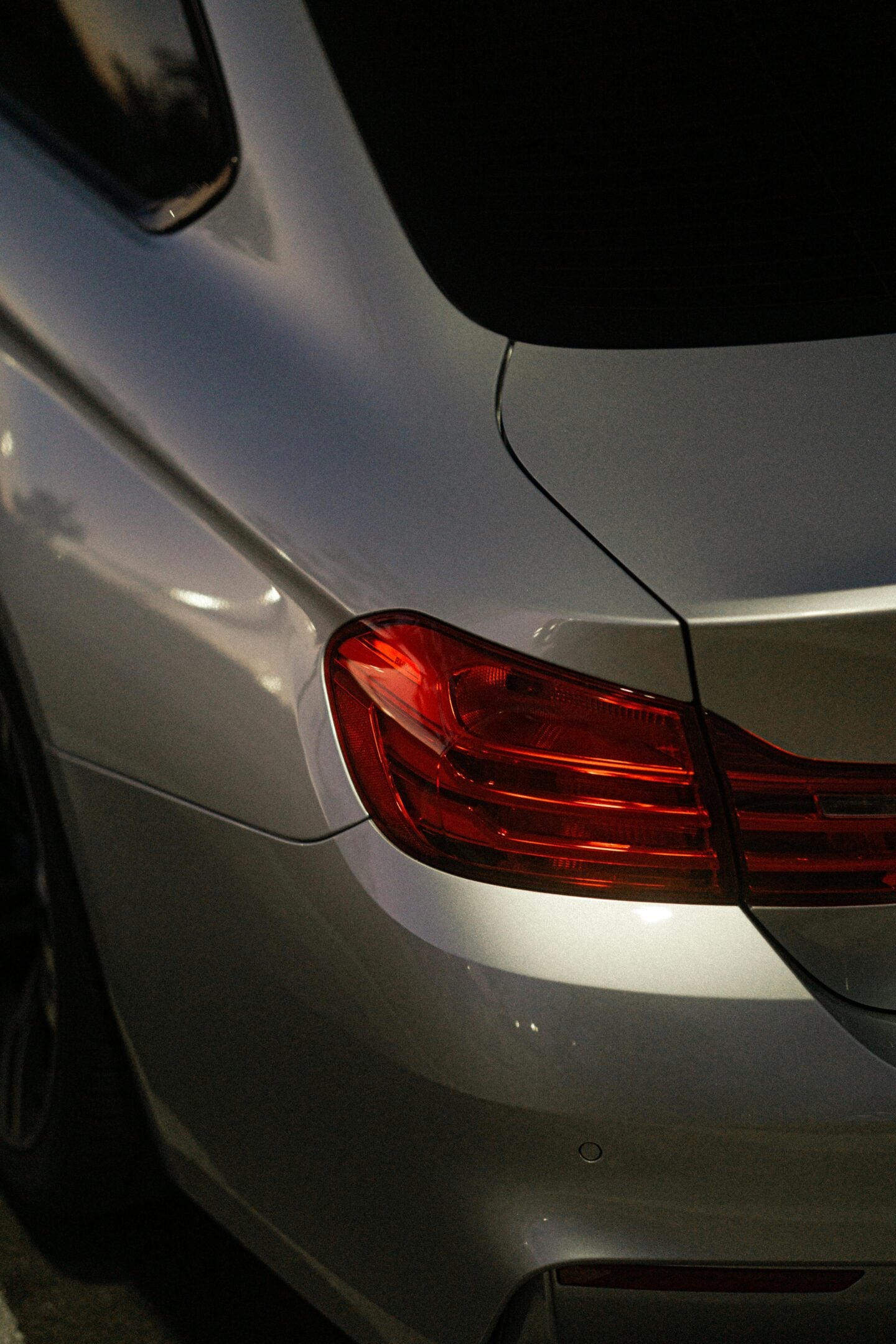 Close-up of the rear section of a silver car, focusing on the sleek red tail light and smooth body lines, captured in low light.