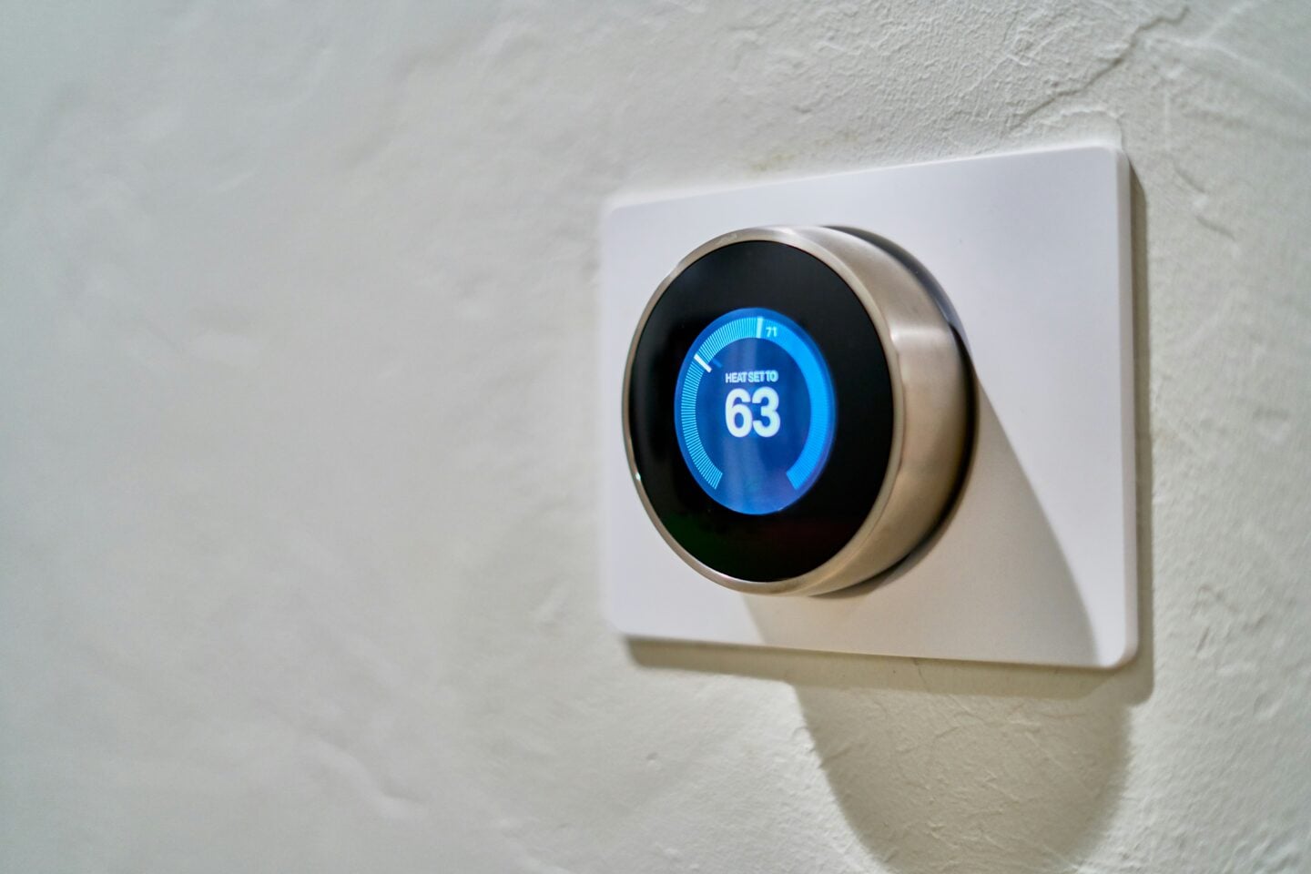 Smart thermostat set to 63 degrees on a textured white wall for efficient home heating control.