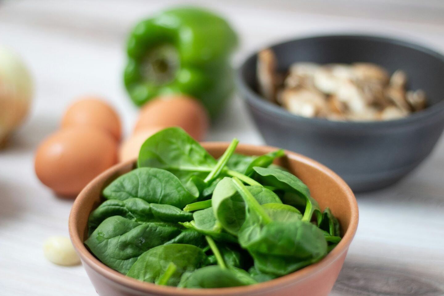 Fresh spinach in a bowl with eggs, green pepper, and mushrooms, highlighting eye-nourishing nutrients.