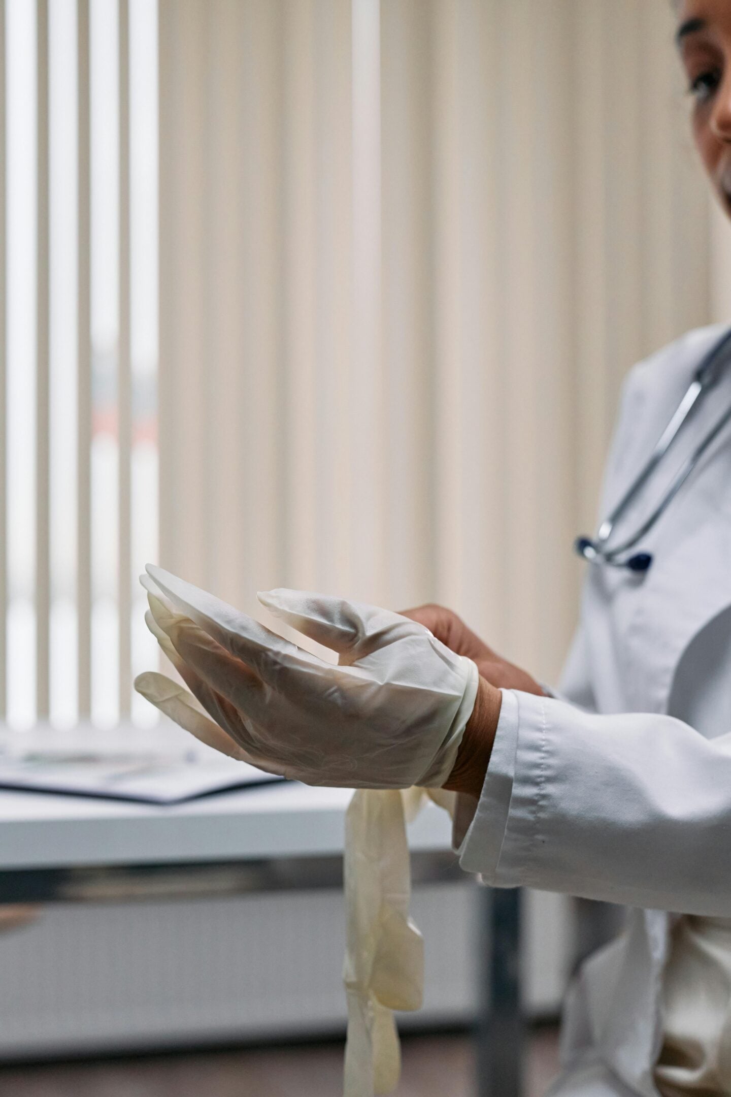 Close-up of a doctor in a white coat and stethoscope putting on medical gloves in a clinic.