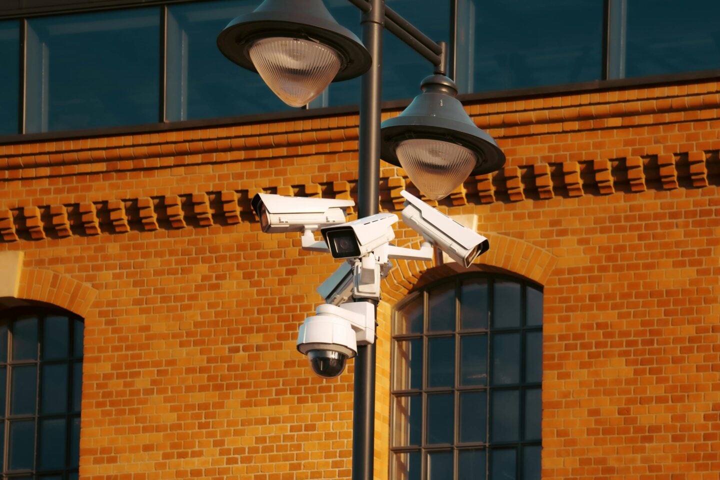 Multiple CCTV security cameras mounted on a pole outside a brick building.
