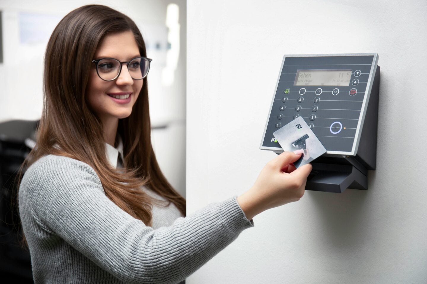 Smiling woman using a key card to access an office security system on the wall.