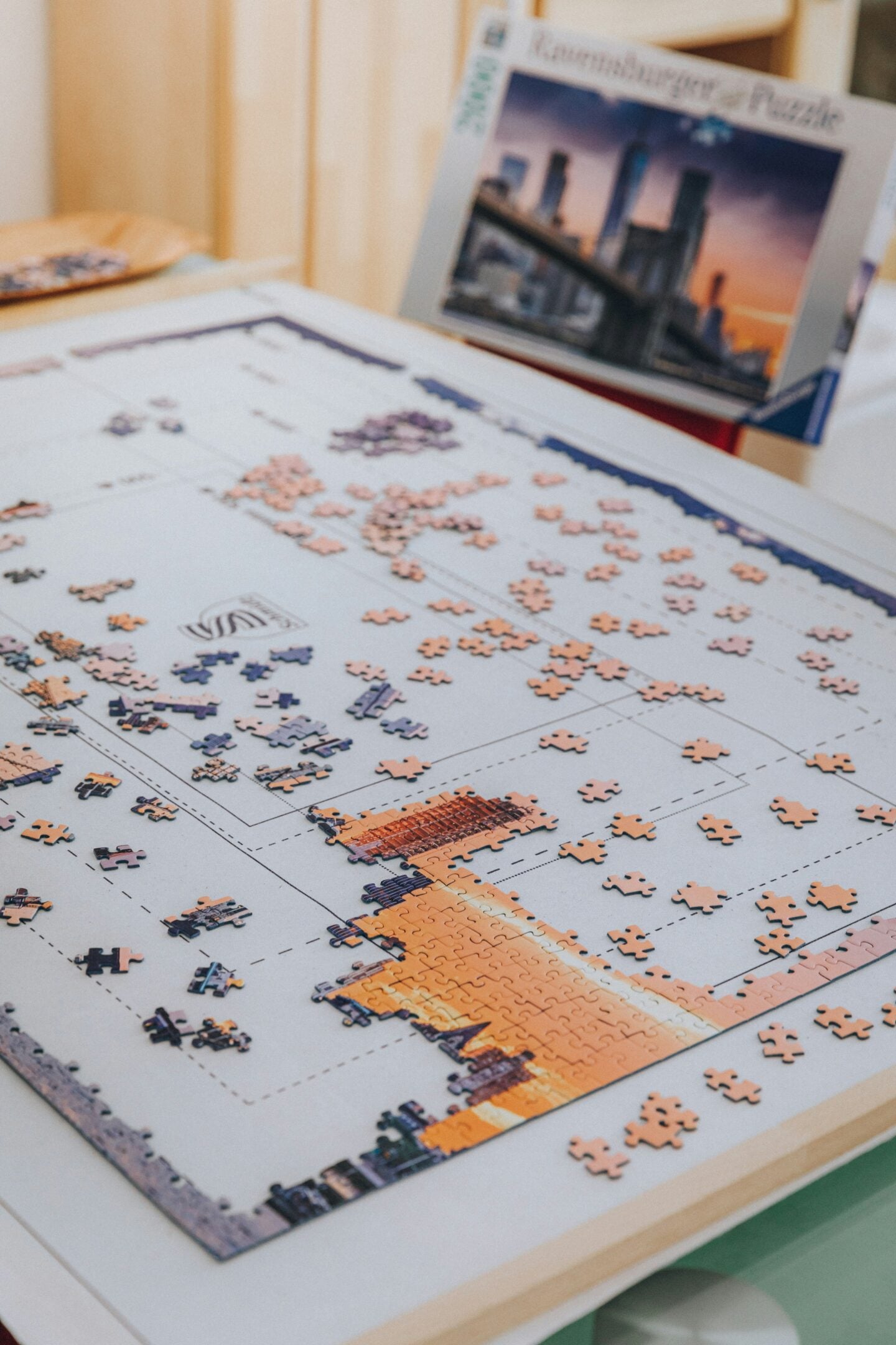 Partially completed jigsaw puzzle of a city skyline spread across a table with puzzle pieces scattered around.