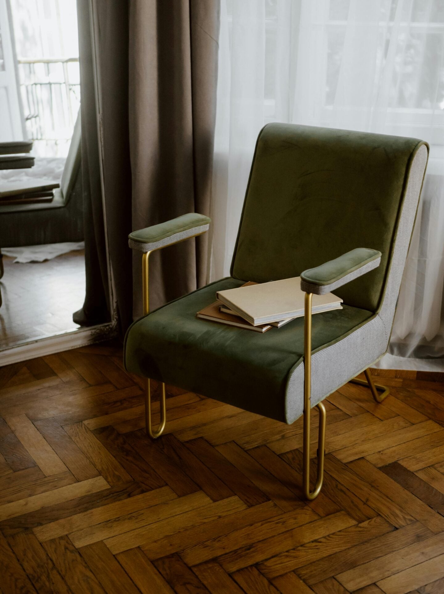 Cozy reading corner with a green velvet chair, books on the seat, and soft natural light through sheer curtains.