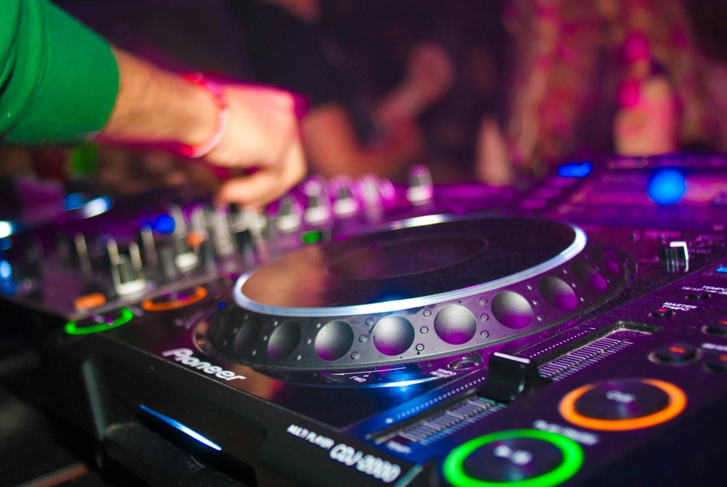 DJ using a Pioneer mixer at a party with colorful lights.
