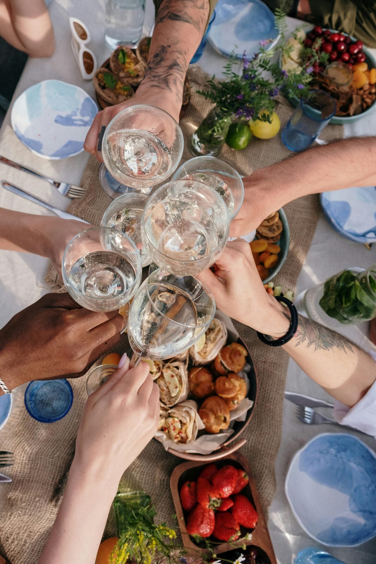 Group of people at brunch raising glasses in a toast over a table filled with food and fruit.