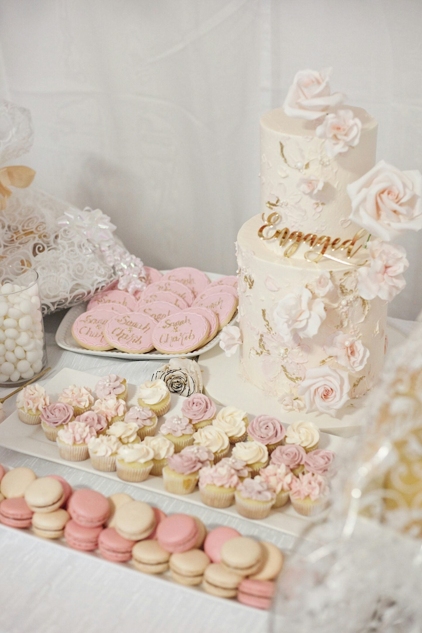 Elegant engagement party dessert table with a floral cake, cupcakes, cookies, and macarons.