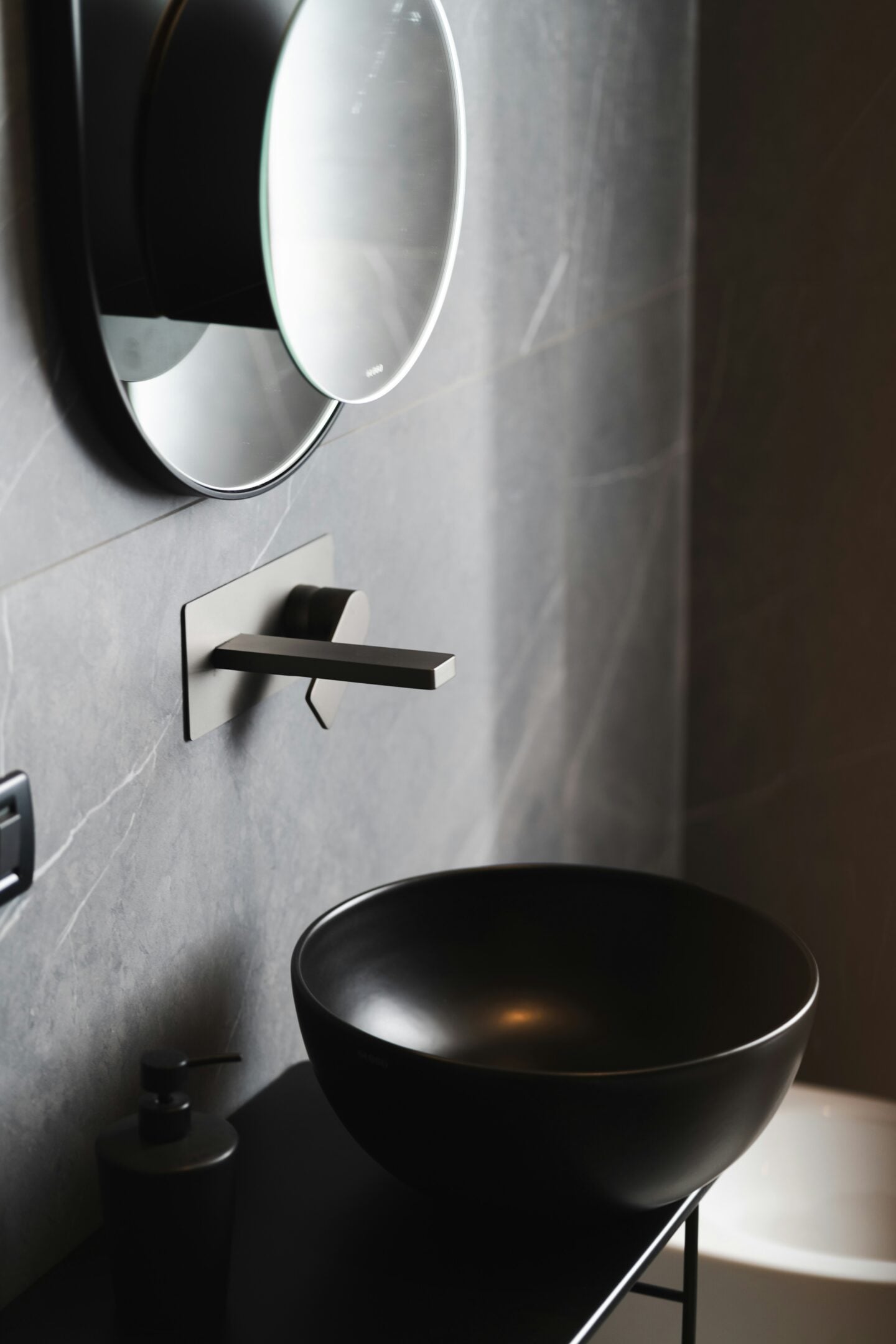Dark modern bathroom with a black round vessel sink, matte black faucet, and double round mirrors.