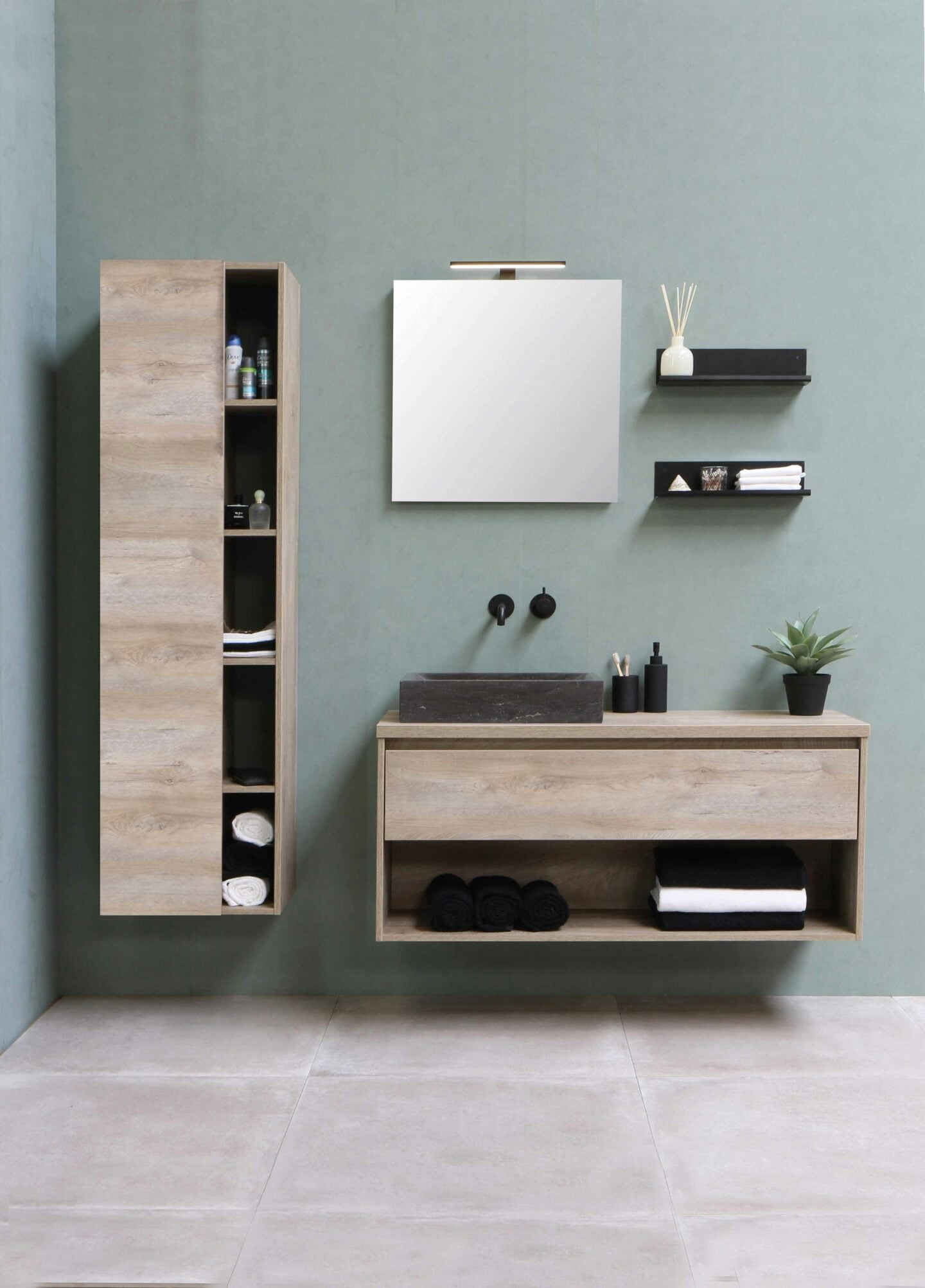 Scandinavian-inspired bathroom with light wood floating cabinets, black fixtures, and minimalist shelving on green walls.