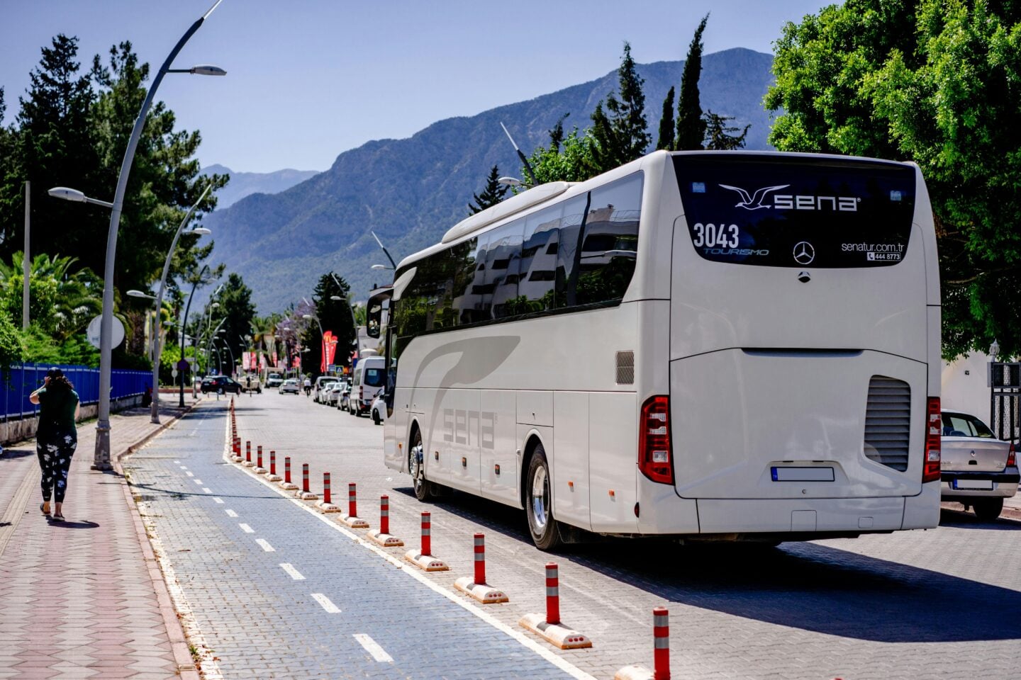 White holiday excursion coach bus driving down a city street with mountains in the background.