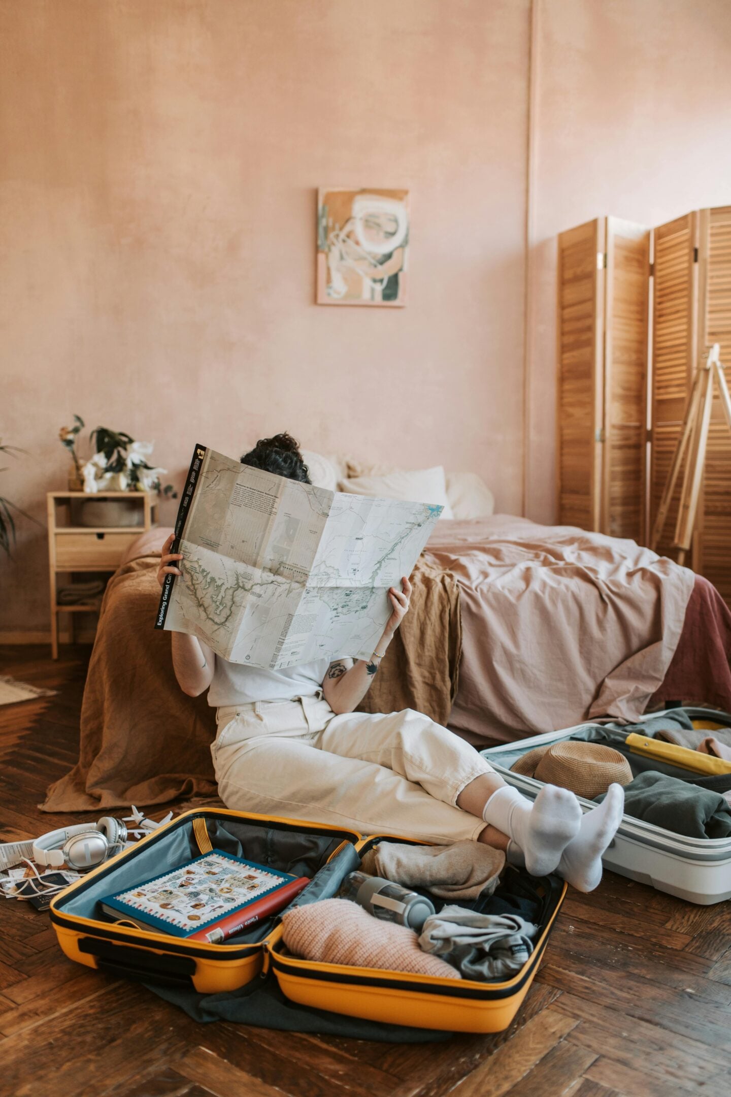 Traveler sitting on the floor reading a map while packing an open suitcase in a cozy bedroom.