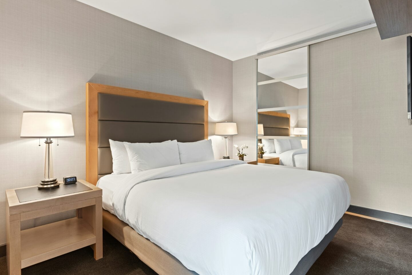 Modern airport hotel room with a neatly made double bed, bedside lamps, and mirrored wardrobe doors.