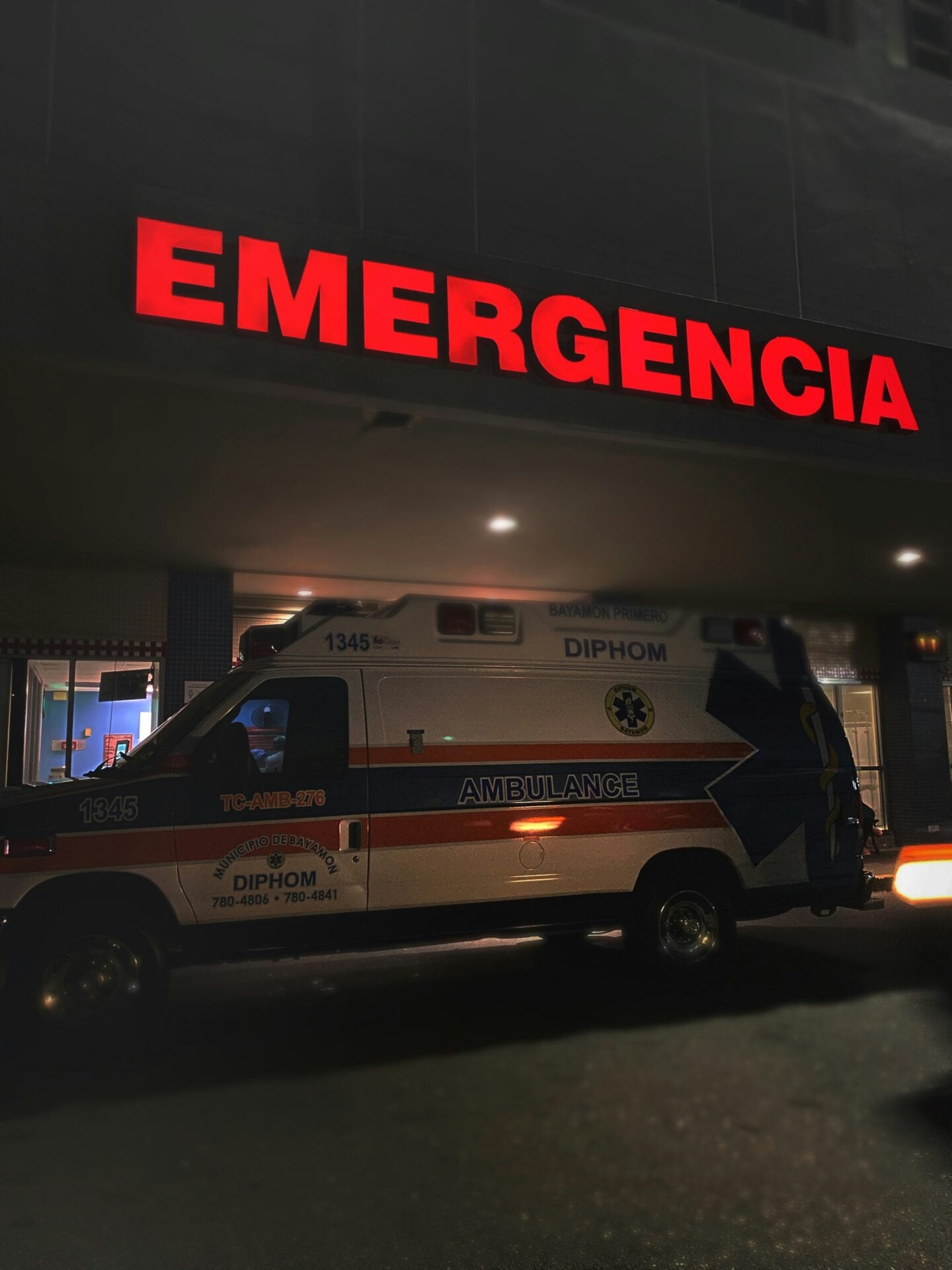 Ambulance parked outside a hospital emergency entrance with a bright red “Emergencia” sign.