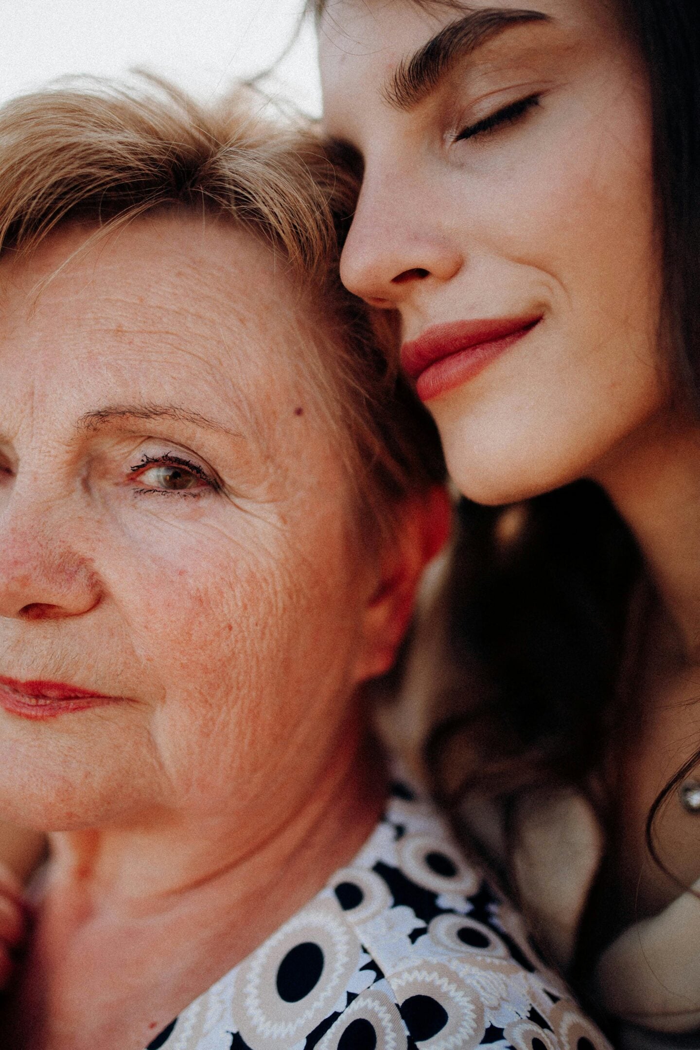 Close-up of an elderly woman with a younger woman leaning affectionately on her shoulder.