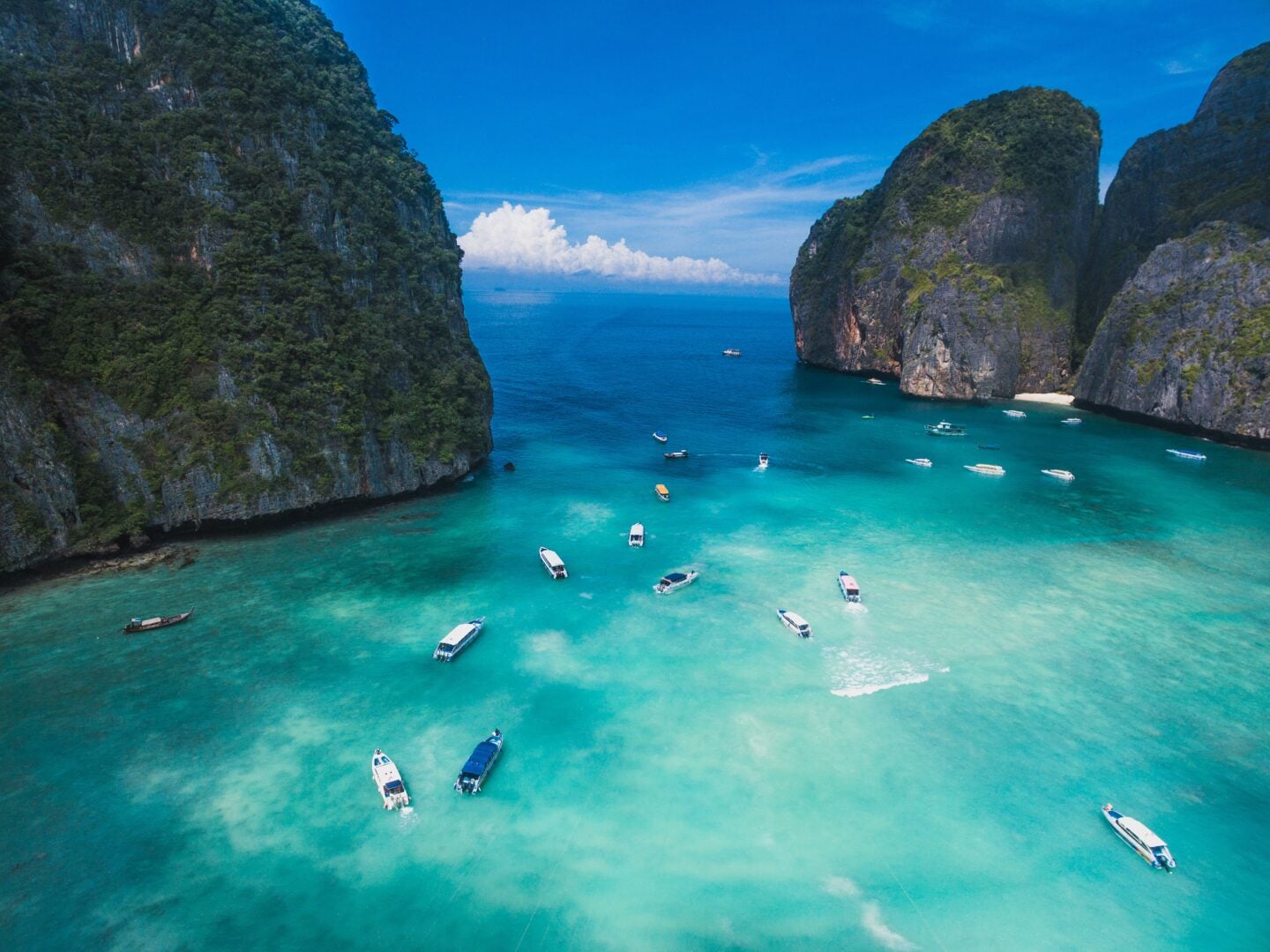 Boats float on clear turquoise water surrounded by dramatic limestone cliffs in Thailand’s Phi Phi Islands.