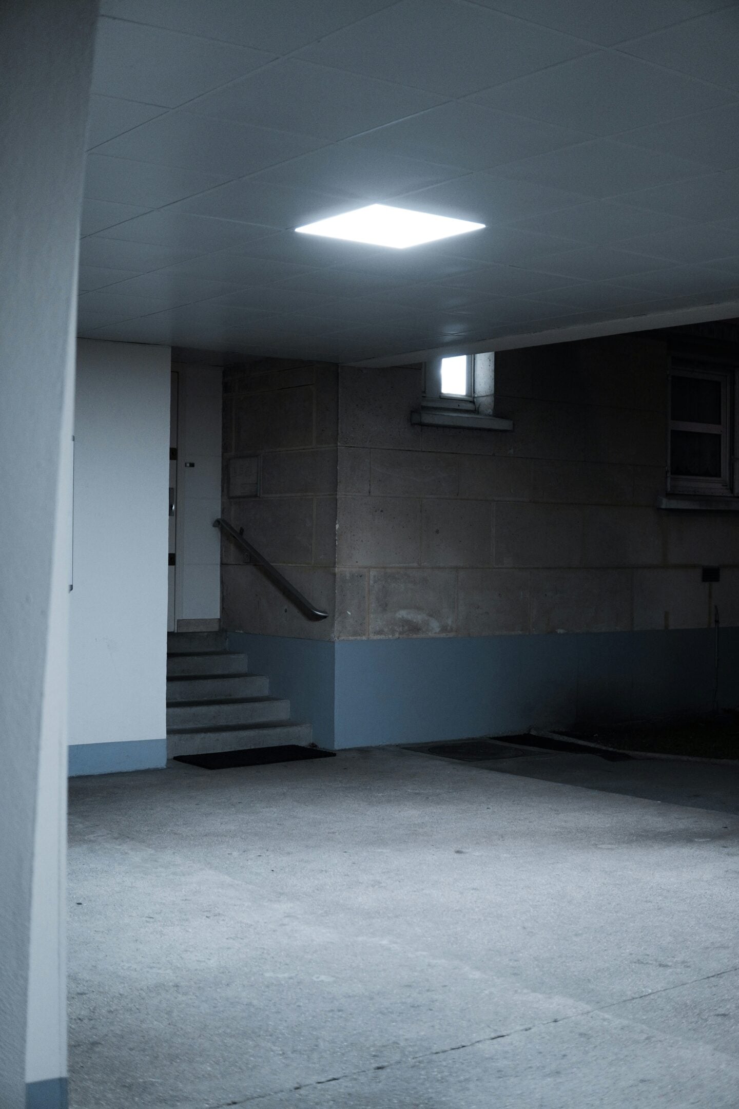 Clean, well-lit basement entry with concrete flooring, a small window, and stairs leading up to the main level.