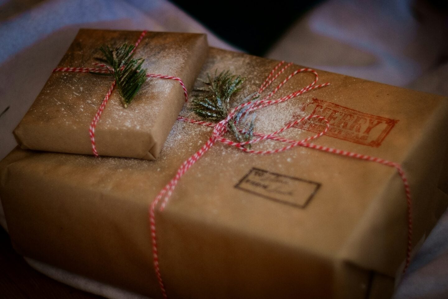 Rustic Christmas presents wrapped in brown paper and twine, decorated with pine sprigs and dusted with snow.