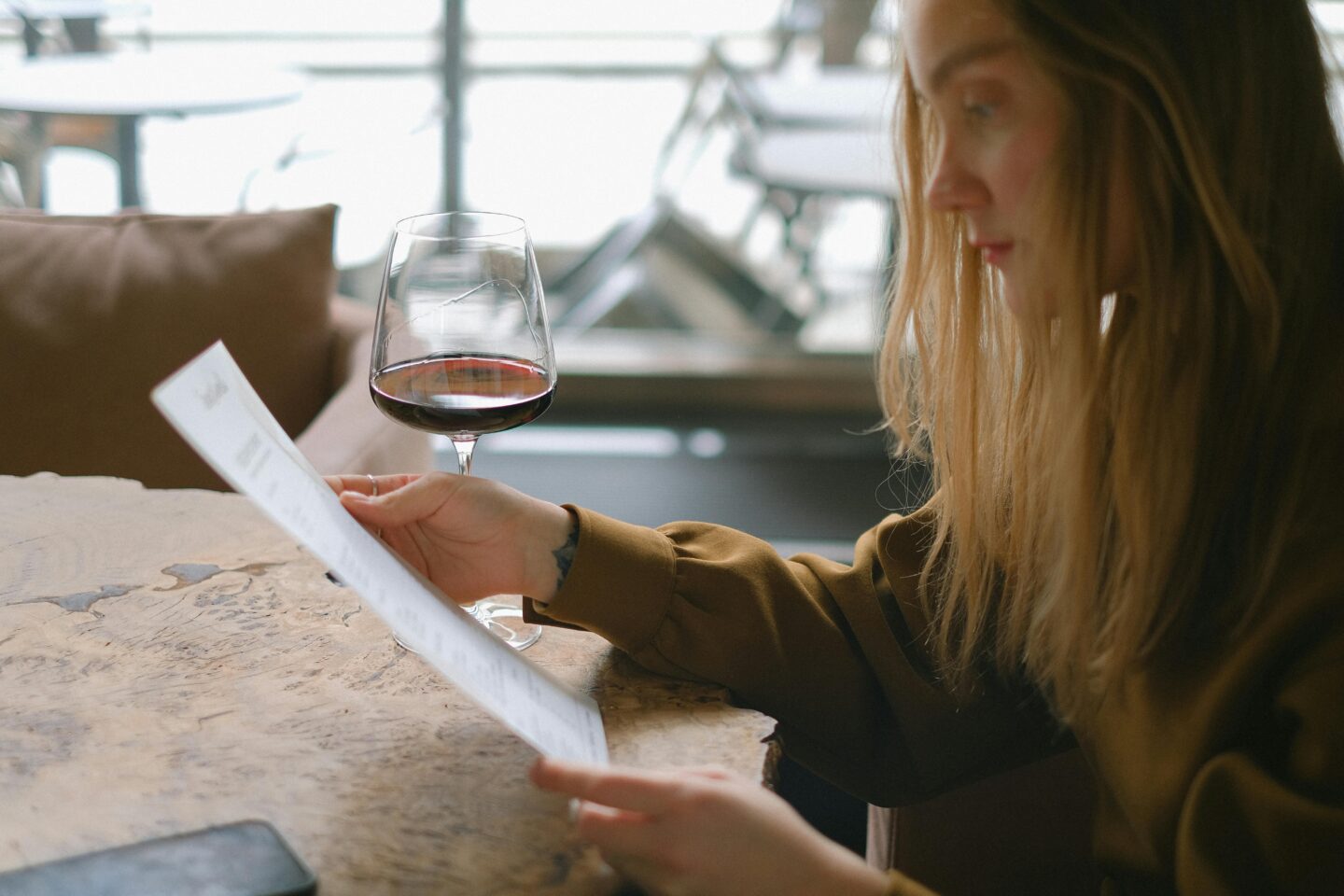Woman reading a menu with a glass of red wine at a steakhouse.