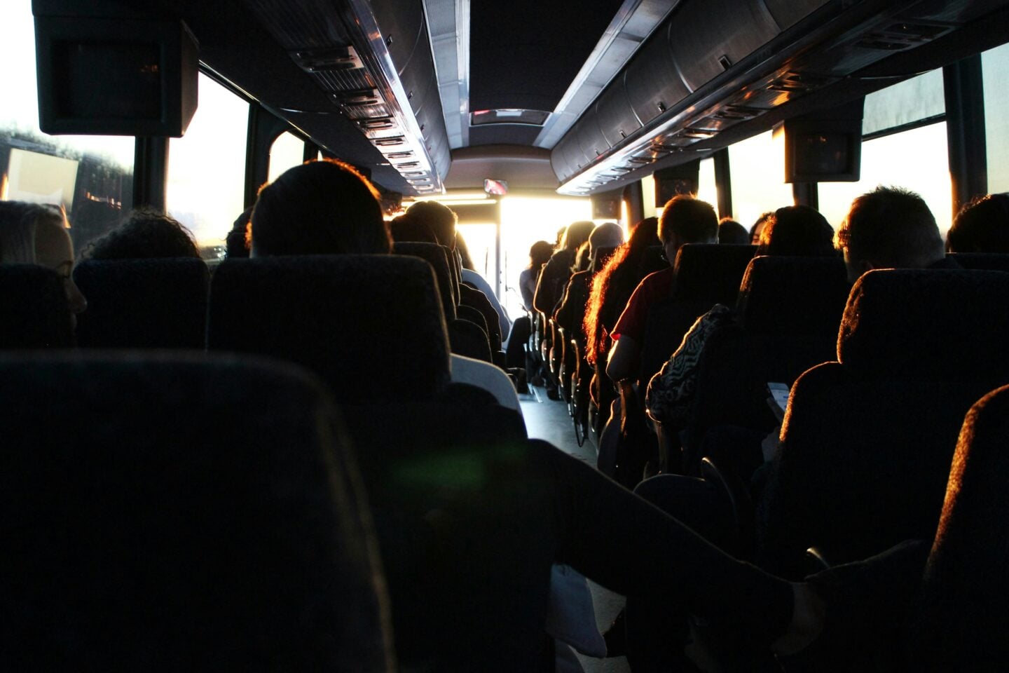 Passengers seated inside a coach bus, with sunlight streaming through the front windows.
