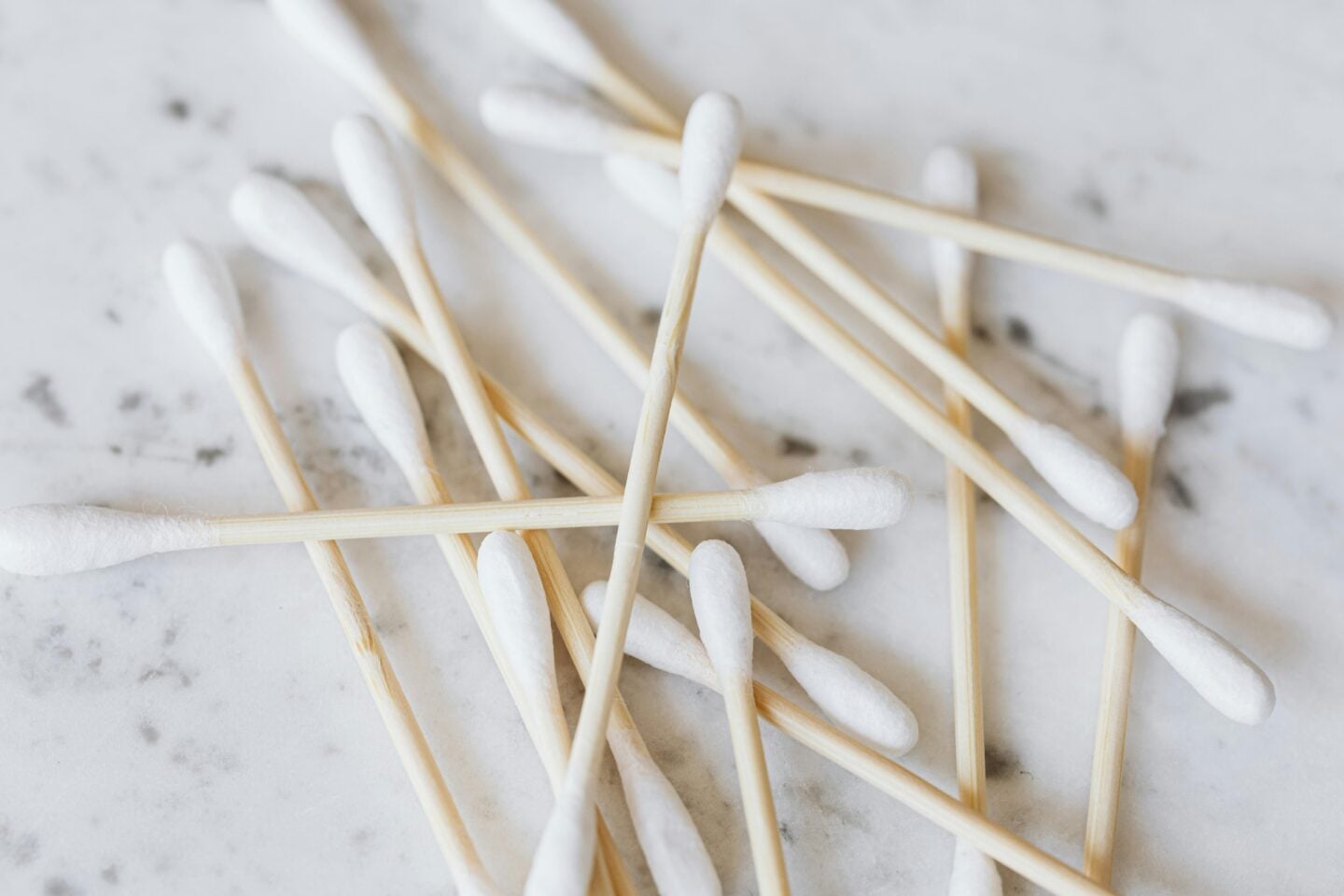 Close-up of biodegradable cotton swabs with wooden sticks scattered on a marble surface.