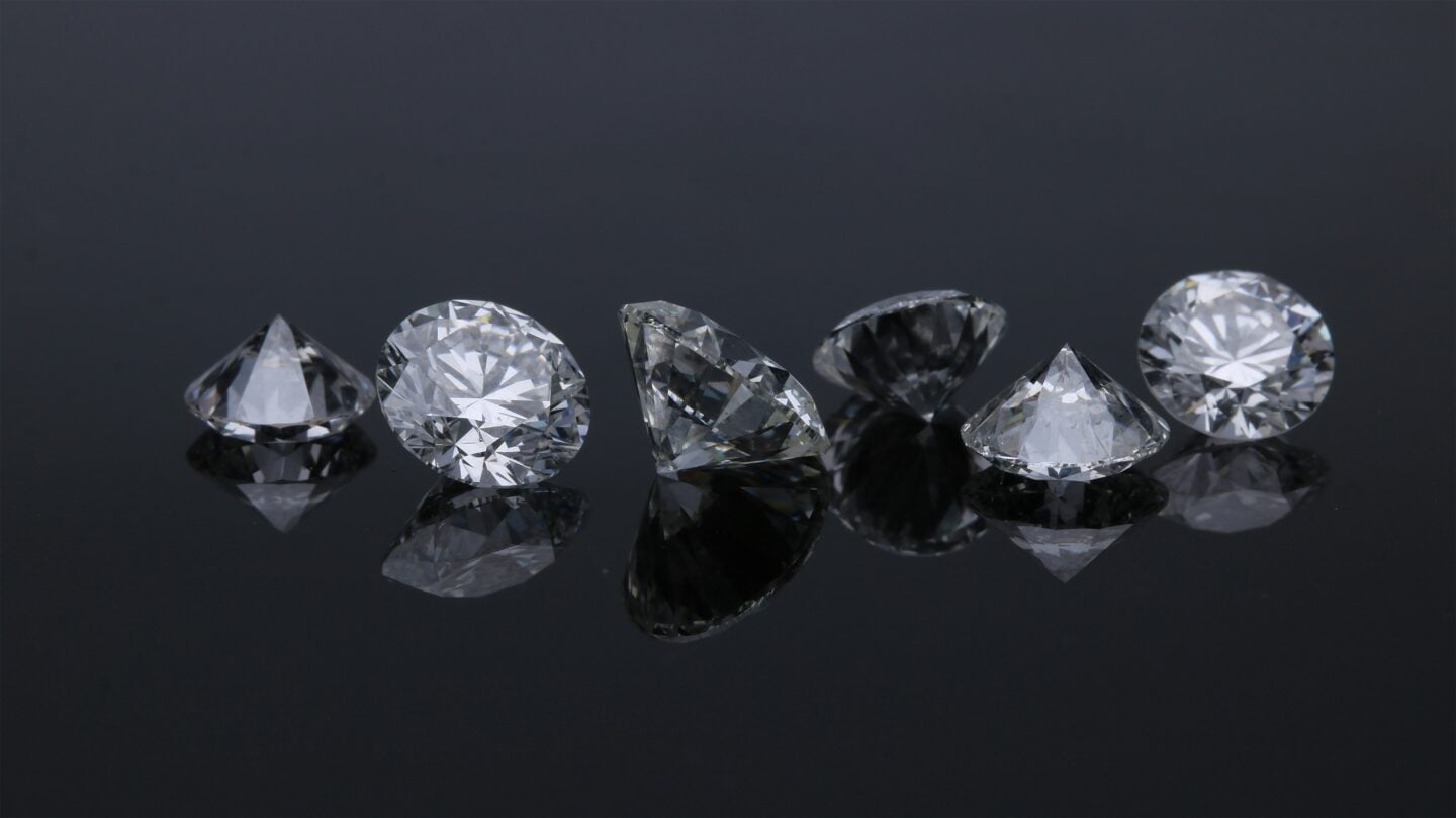 Close-up of loose round brilliant cut diamonds sparkling on a glossy black surface.