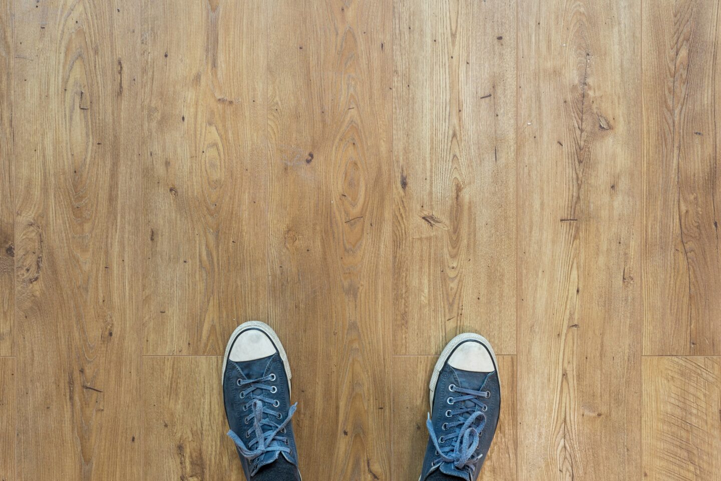 Person wearing sneakers standing on newly installed wood flooring.