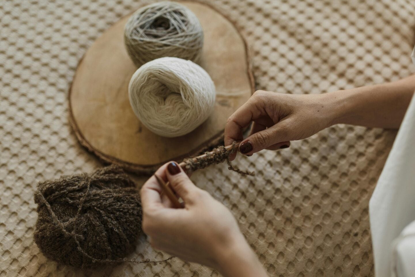 Close-up of hands knitting with natural brown and cream yarn on a wooden tray for a cozy handmade gift.