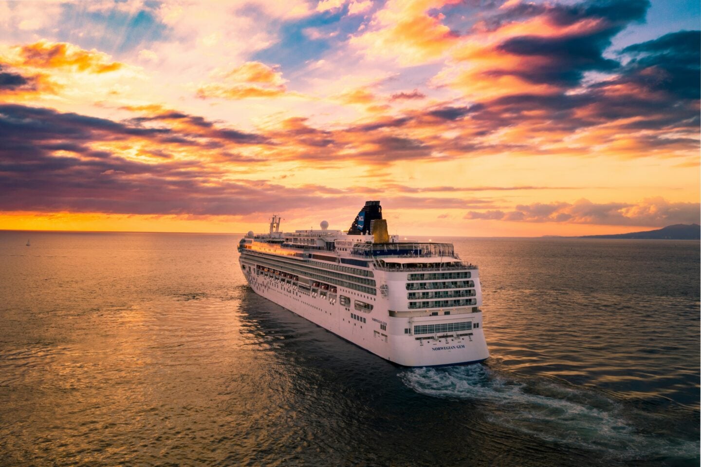Luxury cruise ship sailing at sunset with colorful skies reflecting on the sea.