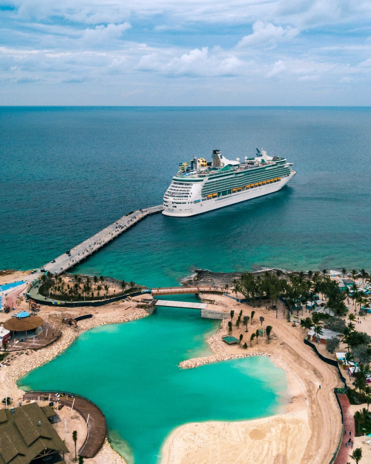 Cruise ship docked at a tropical port with turquoise waters and sandy beaches.