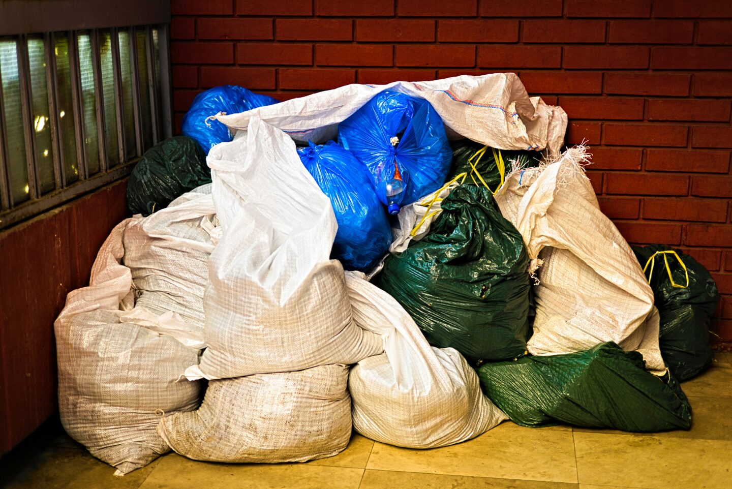 Large pile of garbage bags stacked against a brick wall, representing waste disposal, trash removal services, and junk hauling solutions.